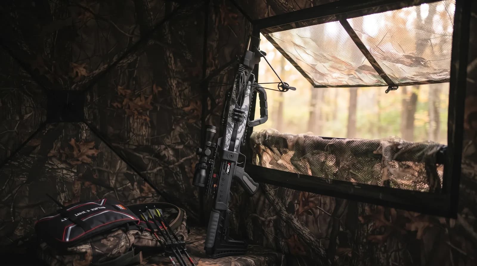 Compact Killer Instinct NEO-X crossbow standing upright beside the window of a ground blind