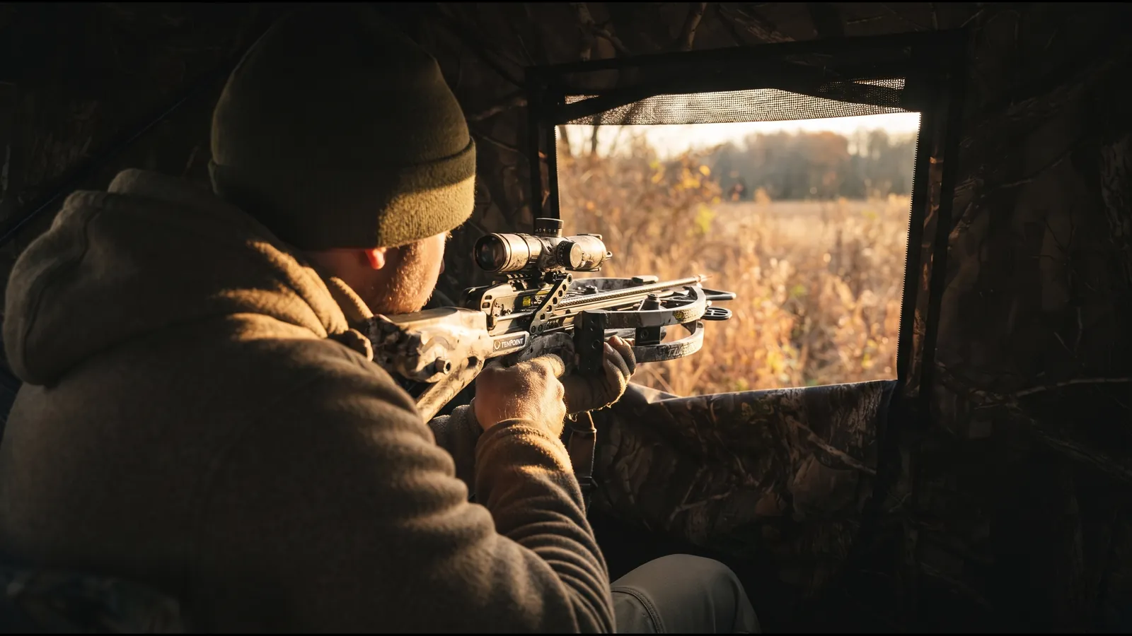 Compact crossbow shouldered inside a pop-up ground blind with fabric walls close on either side