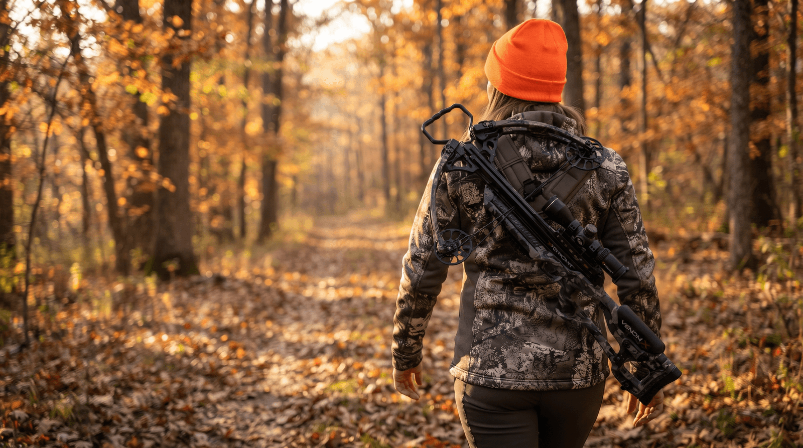 Hunter carrying a light compound crossbow on a sling along an autumn woodland trail