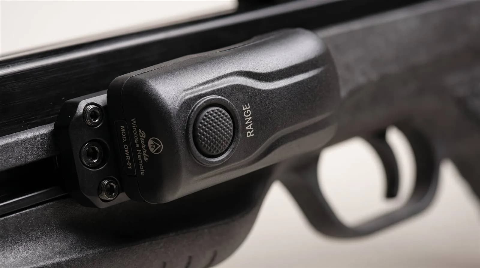 Close-up of the wireless remote switch mounted near the trigger guard of a crossbow, black housing with a single activation button